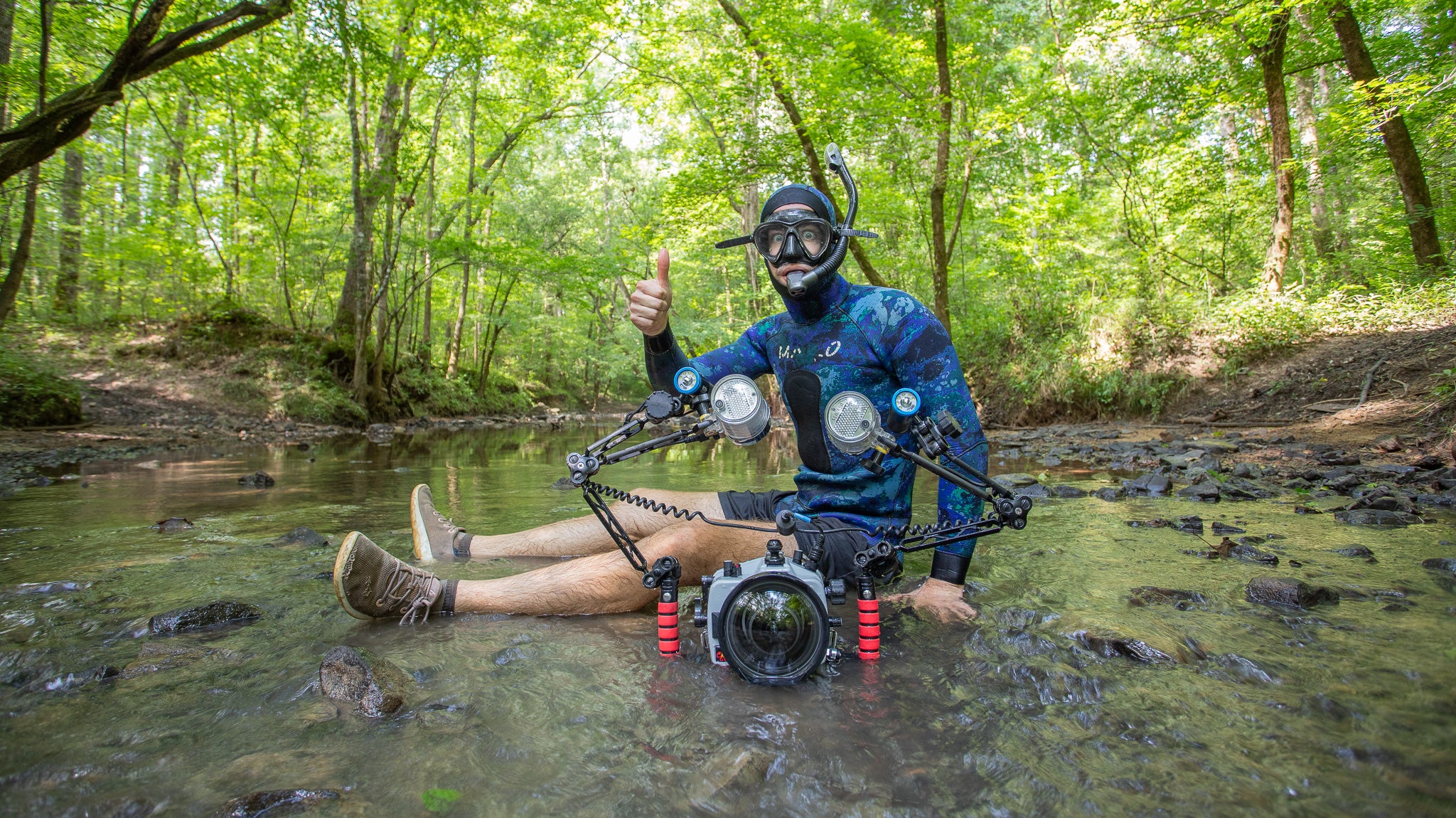 Person with snorkel gear sitting in a creek surrounded by trees